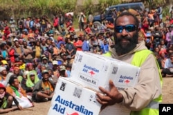 Seorang penduduk desa membawa kotak bantuan Australia saat meninjau kawasan terdampak tanah longsor di desa Yambali, dataran tinggi Papua Nugini Kamis, 20 Juni 2024. (David Kuna/IOM - PNG via AP)