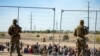 FILE - Migrants wait in line adjacent to the border fence under the watch of the Texas National Guard to enter into El Paso, Texas, May 10, 2023.