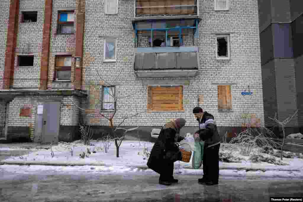 Un voluntario entrega comestibles a una anciana en una de las calles cubiertas de hielo de Lyman. La mayoría de los 20.000 residentes de la ciudad huyeron después&nbsp;que Rusia lanzara la invasión a gran escala&nbsp;deUcrania en 2022. Sólo queda aproximadamente una cuarta parte de la población.