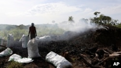 Deo Ssenyimba stands near a heap of burning charcoal in Gulu, Uganda, May 27, 2023. The burning of charcoal is now restricted business across northern Uganda because of the threat of climate change stemming from the uncontrolled felling of trees.