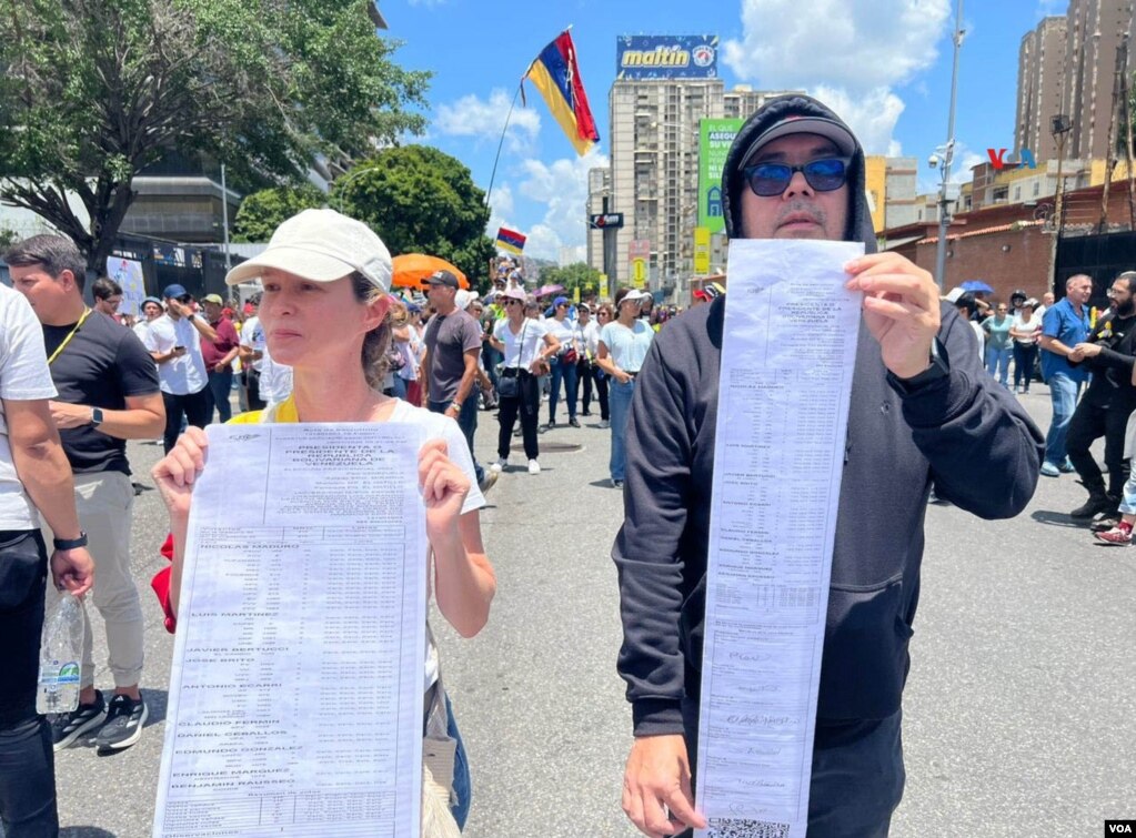 Dos manifestantes muestran réplicas de actas electorales que dan el triunfo al opositor Edmundo González frente al oficialista, el mandatario Nicolás Maduro, tras los comicios del 28 de julio de 2024. [Fotos, VOA].