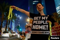 Seorang perempuan memegang poster dan pita-pita kuning dalam demonstrasi di Tel Aviv, Israel oleh para anggota keluarga dan para pendukung sandera yang ditahan oleh Hamas di Gaza, Sabtu, 28 Oktober 2023. (Foto: Ammar Awad/Reuters)