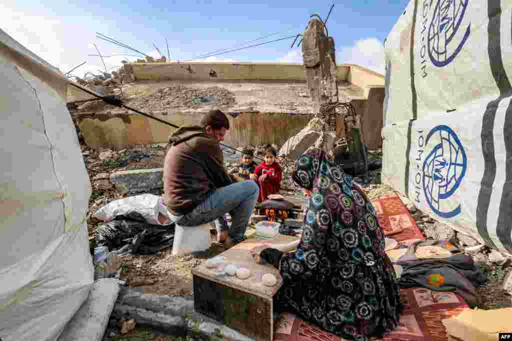 A woman prepares fresh dough for bread as she sits next to a man and children outside tents next to the remains of a destroyed building in Rafah in the southern Gaza Strip.