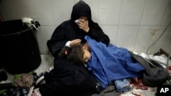A Palestinian woman cries as she sits next to her girl wounded in the Israeli bombardment of the Gaza Strip while receiving treatment at the Nasser hospital in Khan Younis, Southern Gaza Strip, Jan. 22, 2024. 