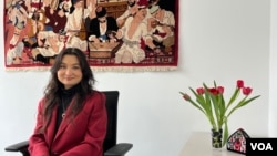 Zumretay Arkin, from the World Uyghur Congress, sits behind the renowned "Uyghur Muqam" painting at the advocacy group's Munich office, March 1, 2024. (VOA/Liam Scott)