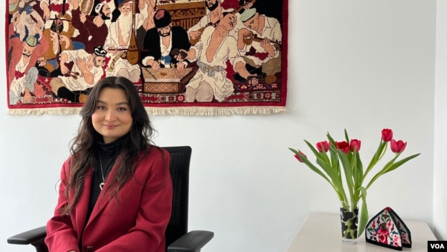 Zumretay Arkin, from the World Uyghur Congress, sits behind the renowned "Uyghur Muqam" painting at the advocacy group's Munich office, March 1, 2024. (VOA/Liam Scott)