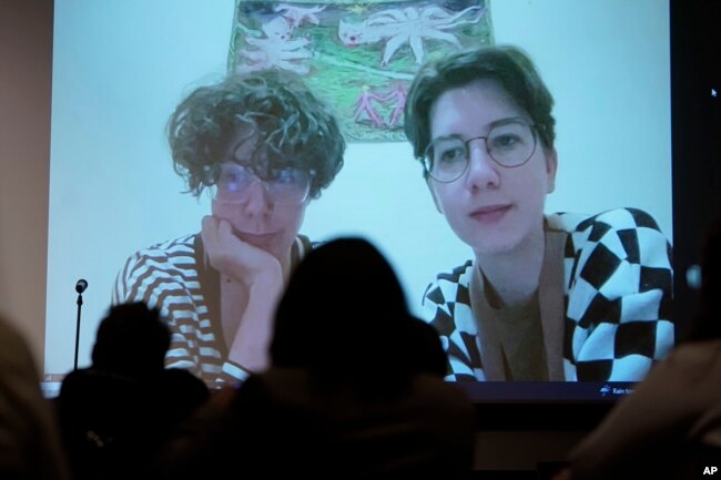 Jenya Polosina, left, Anna Ivanenko, right, both Kyiv, Ukraine-based artists, appear from Kyiv via video link on a screen at an art opening for an exhibit called "Our Fire is Stronger Than Your Bombs" at Saint Anselm College in Manchester, N.H., Monday, May 1, 2023. (AP Photo/Steven Senne)