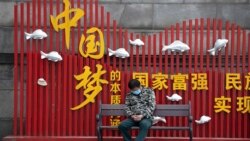 资料照：一名戴着口罩的男子在武汉街头一个中国梦的政府宣传牌下打盹。（2020年4月8日）
