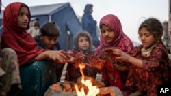 FILE - Displaced Afghan children warm themselves at a fire in a camp near the Torkham Pakistan-Afghanistan border crossing in Torkham, Afghanistan, Nov. 4, 2023, following their repatriation from Pakistan.