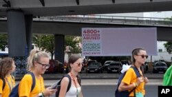 Youths walk by a protest billboard against alleged child abuse by the Catholic Church in Alges, just outside Lisbon, Aug. 2, 2023.