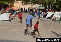 Seorang warga Haiti yang menyelamatkan diri dari serangan geng bermain bersama anaknya di stadiun Vincent yang diubah menjadi kemah pengungsian di Port-au-Prince, Haiti, Rabu, 30 Agustus 2023. (Foto: Richard Pierrin/AFP)