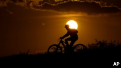 FILE - A cyclist tops a hill on a hot day at sunset, Aug. 20, 2023, in San Antonio. 