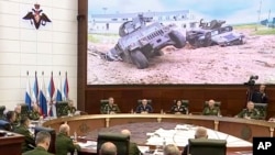 Russian Defense Minister Sergei Shoigu, in front of the flags, speaks with high-level officers in Moscow, May 24, 2023. Damaged allegedly U.S.-made vehicles are seen after fighting in Russia's Belgorod region. (Russian Defense Ministry Press Service via AP)