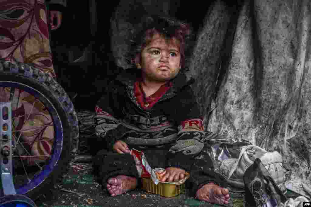 A displaced Palestinian child eats food from a box while sitting in a makeshift tent at a camp beside a street in Rafah on March 13, 2024, amid ongoing battles between Israel and the Hamas militant group. 