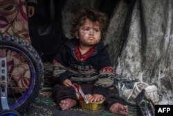 Seorang anak pengungsi Palestina makan makanan dari kotak sambil duduk di tenda darurat di sebuah kamp di samping jalan di Rafah pada 13 Maret 2024, di tengah pertempuran yang sedang berlangsung antara Israel dan Hamas. (Foto: AFP)