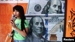 Una mujer bebe jugo junto a una casa de cambio con billetes de dólares estadounidenses impresos en sus ventanas en Buenos Aires, Argentina, 12 de diciembre de 2023. 