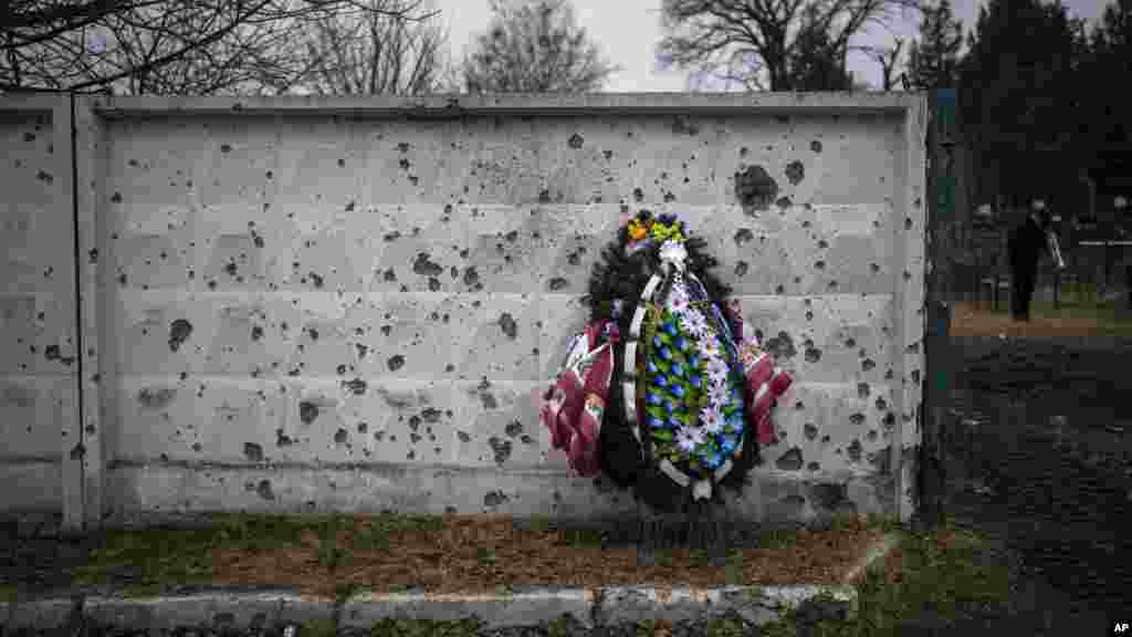 Karangan bunga tampak bersandar di dinding yang rusak akibat pecahan peluru di tempat pemakaman saat seorang perwira brigade Ukraina ke-93 dimakamkan di kota Bucha, dekat Kyiv, Ukraina.