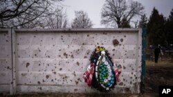 FILE: A wreath leans against a shrapnel-damaged wall in the cemetery where a funeral for an officer of the 93rd Ukrainian brigade was being held in Bucha, near Kyiv, Ukraine. Fri. Feb. 17, 2023. Bucha was the scene of documented mass killings considered to be War Crimes. 