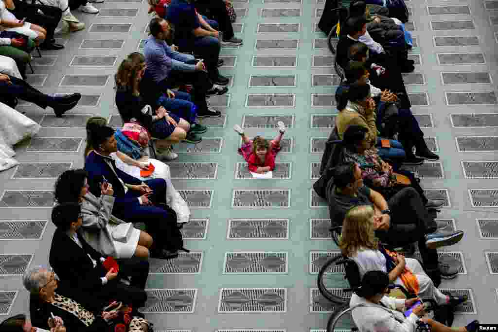 A child lies on the floor as people attend a weekly general audience in the Paul VI hall at the Vatican.