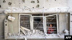 A Palestinian child looks out of the window of a building damaged in an Israeli strike on the Nuseirat refugee camp in the central Gaza Strip, July 6, 2024. 