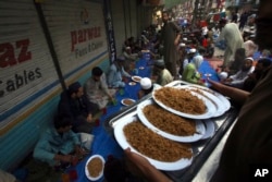 People receives free food plates distributed by volunteers for breaking their fast at a market, in Peshawar, Pakistan, April 16, 2023.