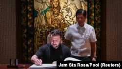 乌克兰总统泽连斯基在菲律宾总统马科斯的注视下在马尼拉的马拉坎南宫贵宾来访簿上签名。（2024年6月3日）