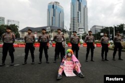 Seorang aktivis memegang plakat duduk di depan polisi dalam aksi Global Climate Strike, memprotes perubahan iklim di kompleks Monumen Nasional (Monas) di Jakarta, 3 Maret 2023. (REUTERS/Willy Kurniawan)