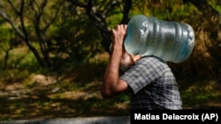 (FILE) A man carries a container with water he collected from a mountain runoff.