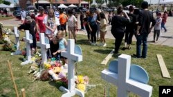Jessica Himes, kneeling in front of cross, and her family look at a memorial by the mall where several people were killed in Saturday's mass shooting in Allen, Texas, May 8, 2023.