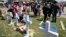 Jessica Himes, kneeling in front of cross, and her family look at a memorial by the mall where several people were killed in Saturday's mass shooting in Allen, Texas, May 8, 2023.