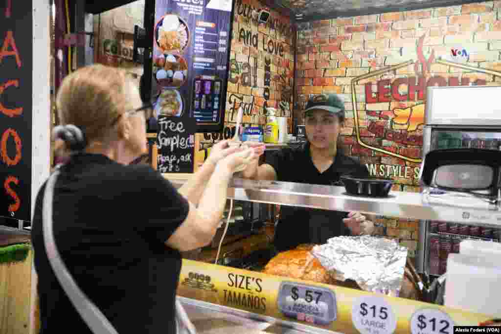 María Paula Solina, integrante del equipo de Lechona La Colombiana, departe con una cliente ocasional que se acerca al puesto de venta, en el&nbsp;Yellow Green Farmers Market, en Hollywood, Florida, el sábado 10 de junio de 2023.&nbsp;