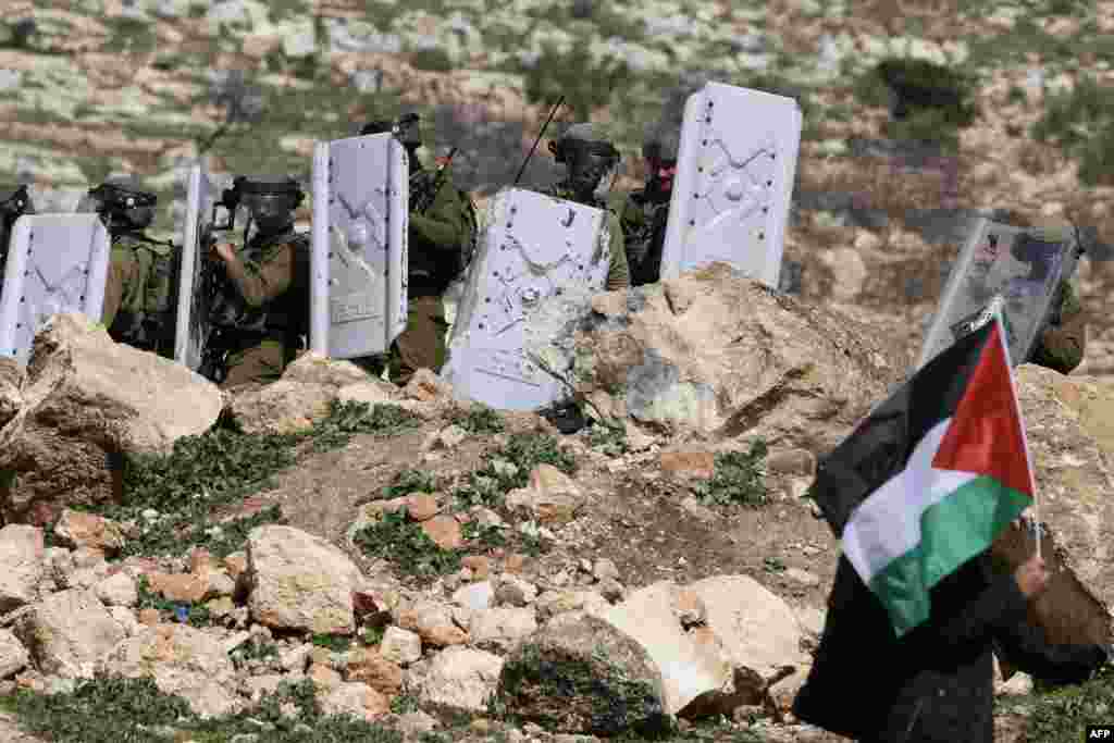 Seorang pria Palestina mengibarkan bendera di dekat pasukan keamanan Israel selama aksi demonstrasi menentang pos terdepan Israel di kota Nablus, Tepi Barat yang diduduki Israel.