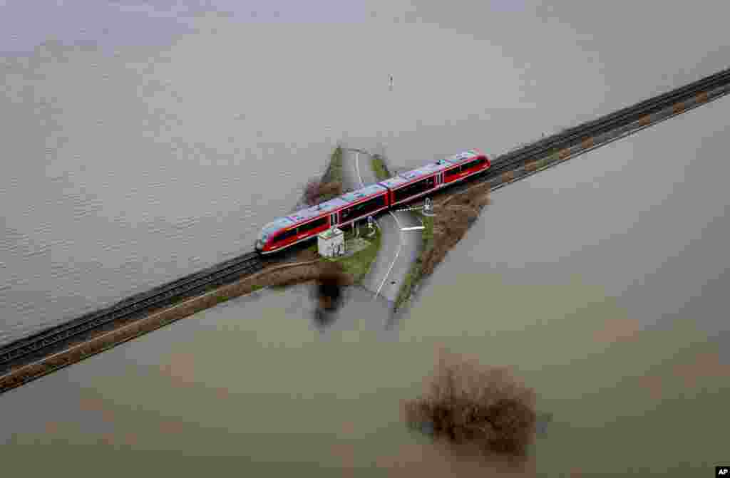 A train passes a railroad crossing between flooded fields in Nidderau-Eichen near Frankfurt, Germany, Jan. 16, 2023.