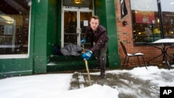 Mikey Reynolds, an employee at The Works on Main Street in Brattleboro, Vt., shovels the sidewalk in front of the restaurant as a person sleeps in the doorway on March 23, 2024. 