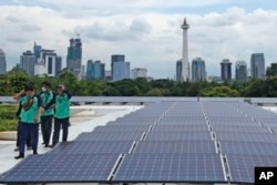 FILE - Workers walk near solar panels that provide partial electrical power to Istiqlal Mosque as the city skyline is seen in the background, in Jakarta, Indonesia, Wednesday, March 29, 2023.