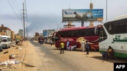 People wait next to passenger buses as smoke billows in an area in Khartoum where fighting continues between Sudan's army and paramilitary forces, April 28, 2023.