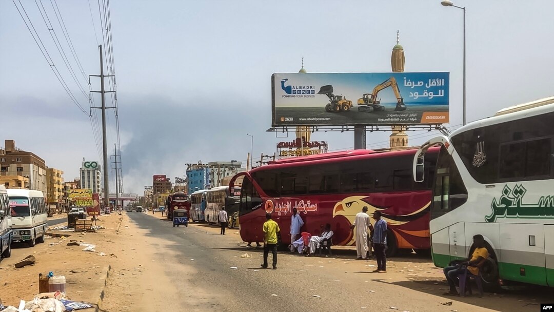 People wait next to passenger buses as smoke billows in an area in Khartoum where fighting continues between Sudan's army and paramilitary forces, April 28, 2023.