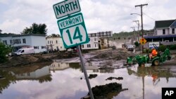 FILE - A small tractor clears water from a business as flood waters block a street, July 12, 2023, in Barre, Vt.