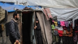 A Palestinian man walks past as a woman stands at the entrance of a tent in an area housing displaced people in Rafah, in the southern Gaza Strip, on April 30, 2024.