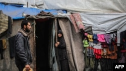 A Palestinian man walks past as a woman stands at the entrance of a tent in an area housing displaced people in Rafah, in the southern Gaza Strip, on April 30, 2024.