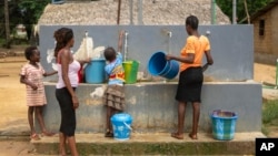 ARCHIVO - Personas recogen agua de una bomba comunitaria en su aldea de Tshiende, afectada por la extracción de petróleo, en Moanda, República Democrática del Congo, el 23 de diciembre de 2023.