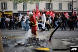 A firefighter hoses down burnt debris which was set alight, as protesters march past during a May Day (Labor Day) rally, marking International Workers' Day, in Paris, on May 1, 2024.