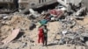 A Palestinian child walks with a stuffed bear recovered from the rubble of a destroyed building following Israeli bombardment in Khan Yunis on June 21, 2024.