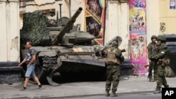 Russian servicemen guard an area standing in front of a tank in a street in Rostov-on-Don, Russia, June 24, 2023. 