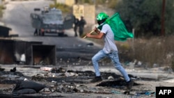 A Palestinian youth holds a Hamas flag during confrontations with Israeli troops at the northern entrance of Ramallah, West Bank, near the Israeli settlement of Beit El, Oct. 27, 2023, as battles continue between Israel and Hamas.