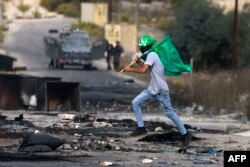 Seorang remaja Palestina memegang bendera Hamas dalam bentrokan dengan tentara Israel di pintu masuk utara Ramallah, di Tepi Barat, dekat permukiman Israel Beit El di tengah konflik Israel dan Hamas, Jumat, 27 Oktober 2023. (Foto: Jaafar Ashtiyeh/AFP)