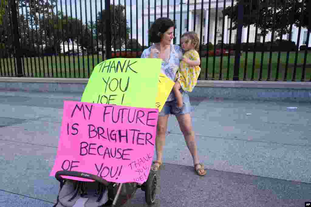 Anna Filipic sostiene a su hija Louisa, junto a pancartas en apoyo al presidente Biden en su decisión de dejar la carrera por la reelección. En las cartulinas se lee en inglés: &quot;Gracias Joe. Mi futuro es más brillante debido a ti&quot;.&nbsp;