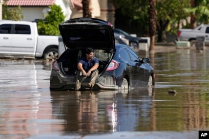 Dorian Padilla sits in his car as he waits for a tow after he got stuck in the mud on a street Cathedral City, California, Aug. 21, 2023.
