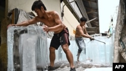 Workers move blocks of ice into a storage unit at a fresh market during a heatwave in Bangkok on April 25, 2023.