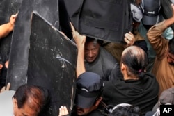 Security personnel hold bulletproof shields to secure former Prime Minister Imran Khan, center, after appearing in a court, in Lahore, Pakistan, March 21, 2023.